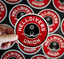 Load image into Gallery viewer, Round sticker with black white and red design with two white sling blades and a white star surrounded by the words Helldivers Union
