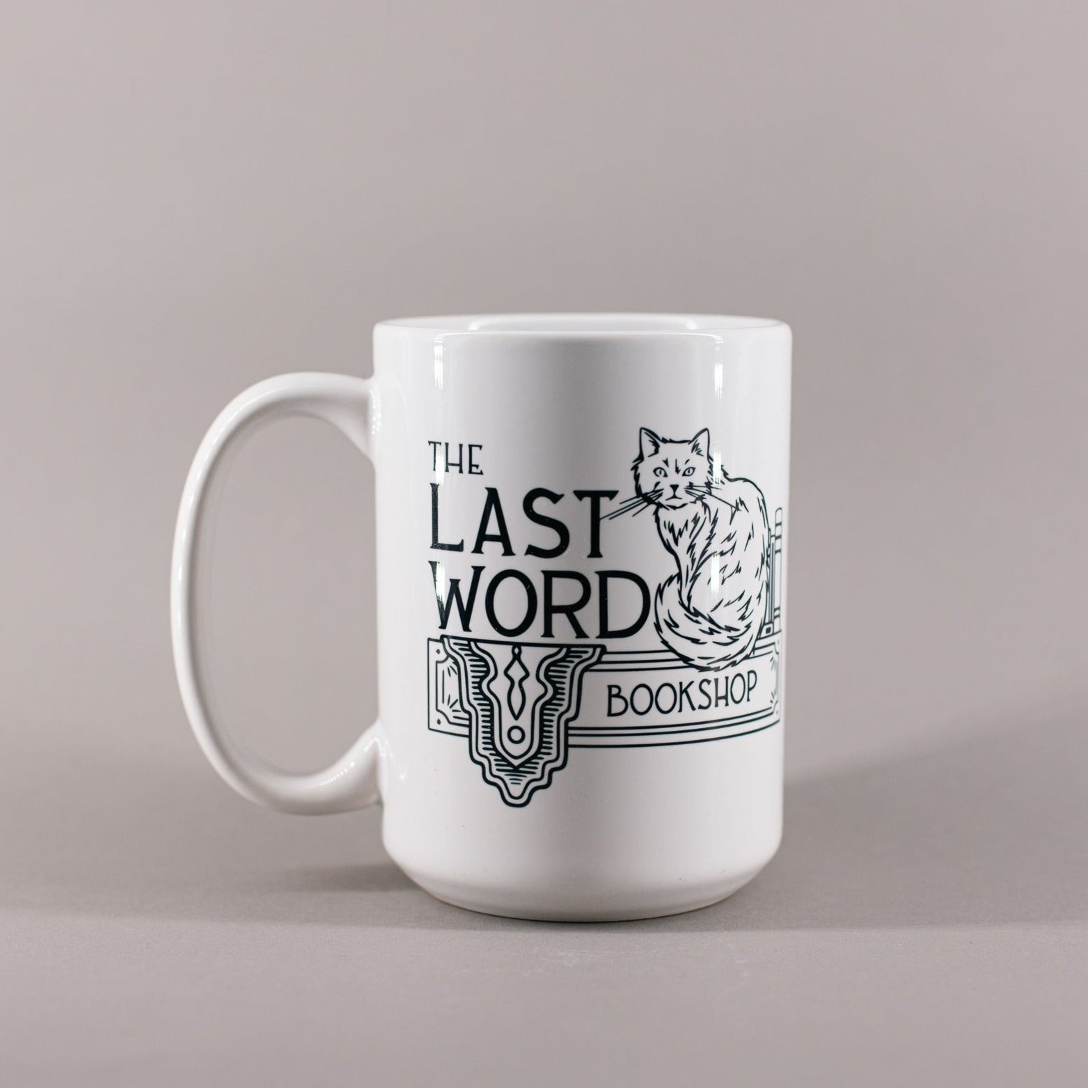 White mug that says The Last Word Bookshop and has a fluffy cat sitting next to books