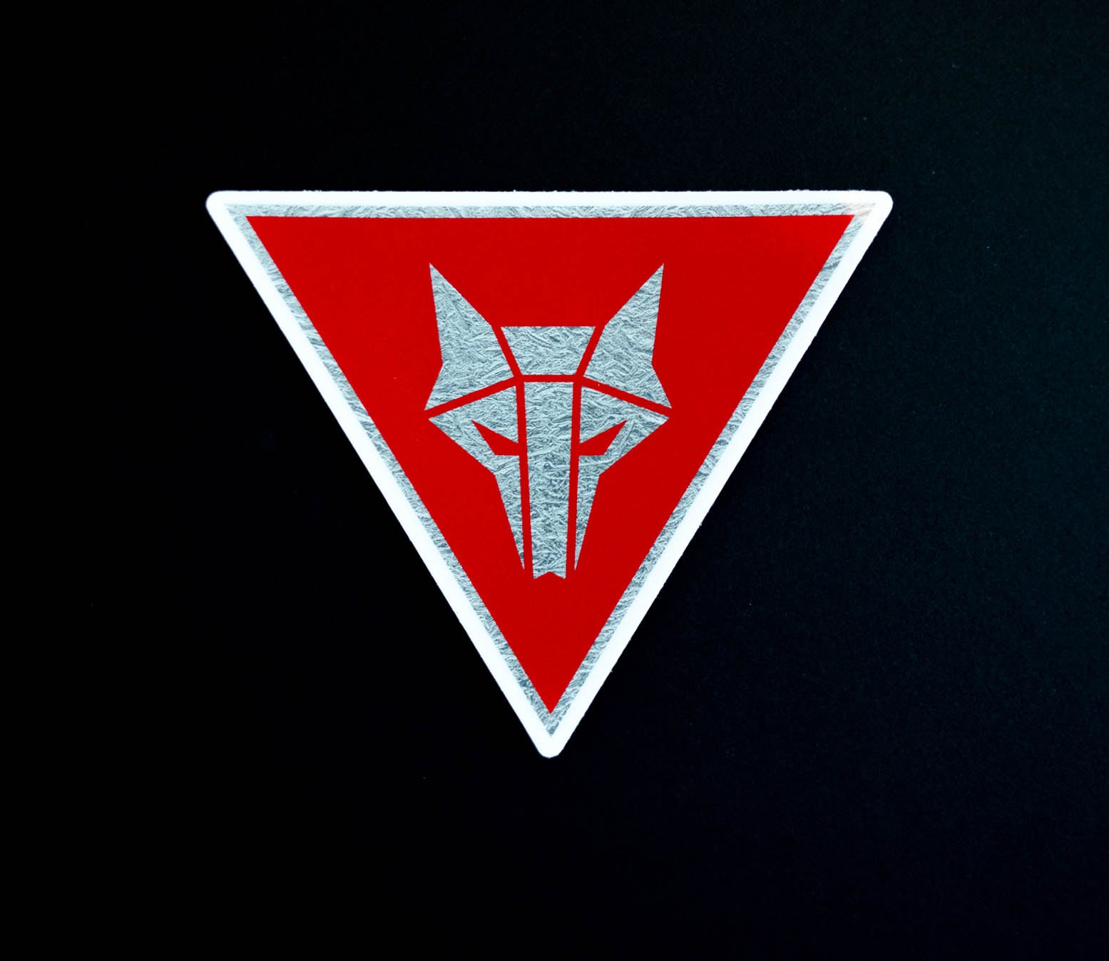 Inverted triangle shaped sticker with red background and a silver Howler sigil in the center