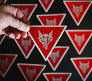 Inverted triangle shaped sticker with red background and a silver Howler sigil in the center