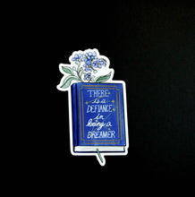 Load image into Gallery viewer, Sticker with blue flowers inside a hardcover blue book with &quot;there is defiance in being a dreamer&quot; and a constellation with seven stars 
