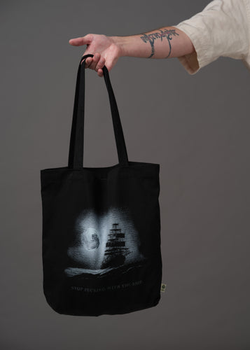 Black tote with a pirate ship on the ocean under a full moon and text that reads 'Stop fucking with the ship' 
