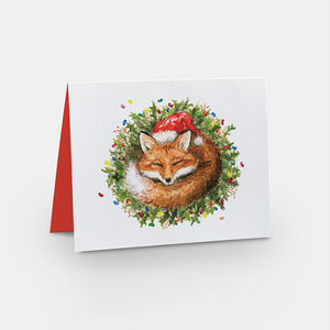 Card with white background and a red fox wearing a Santa hat curled up in a green wreath covered in jellybeans 