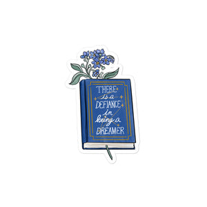 Sticker with blue flowers inside a hardcover blue book with "there is defiance in being a dreamer" and a constellation with seven stars 