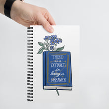 Load image into Gallery viewer, Spiral notebook with white background, blue flowers in a book that says &quot;there is a defiance in being a dreamer&quot;
