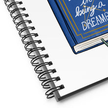 Load image into Gallery viewer, Spiral notebook with white background, blue flowers in a book that says &quot;there is a defiance in being a dreamer&quot;
